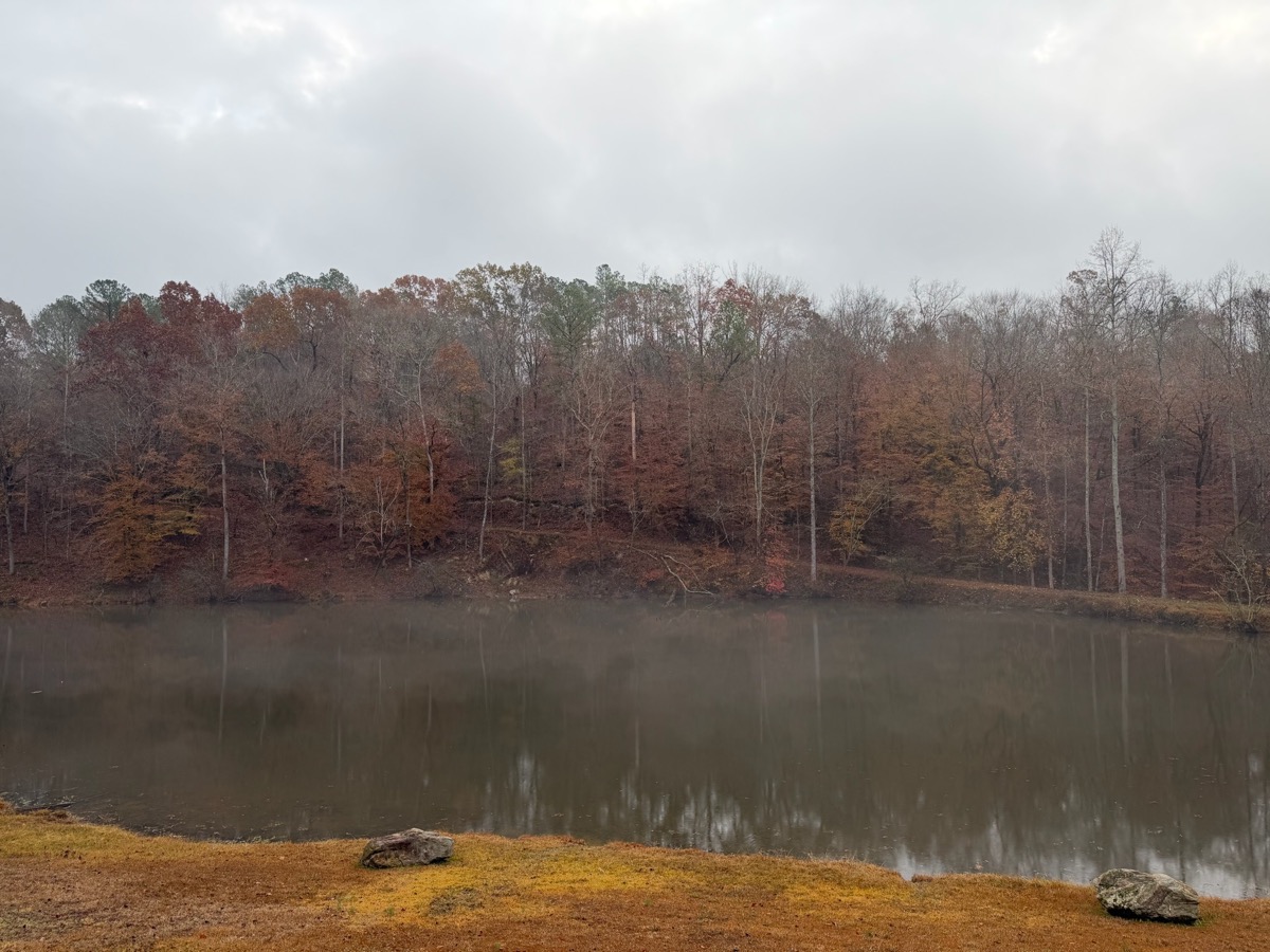 On-property pond in fall with red and orange foliage reflected in calm water